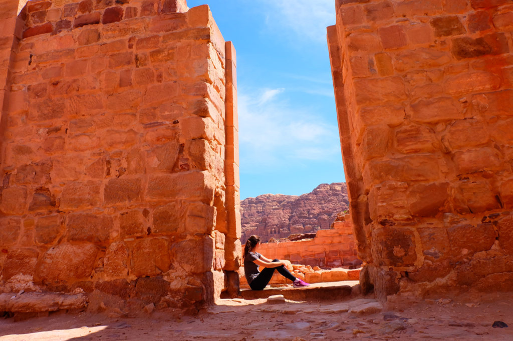 My tips for solo travel for women. Photo of girl sitting in ruins in Petra, Jordan.