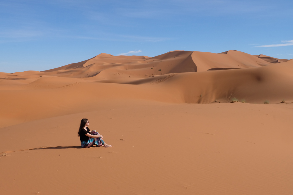 Girl in Sahara Desert in Morocco sitting on the sand.