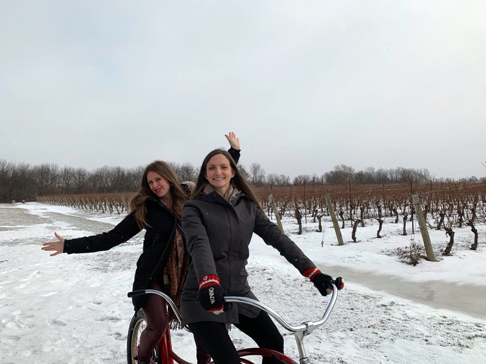 Two girls on a stationary bike in a winter ice wine vineyard in NOTL