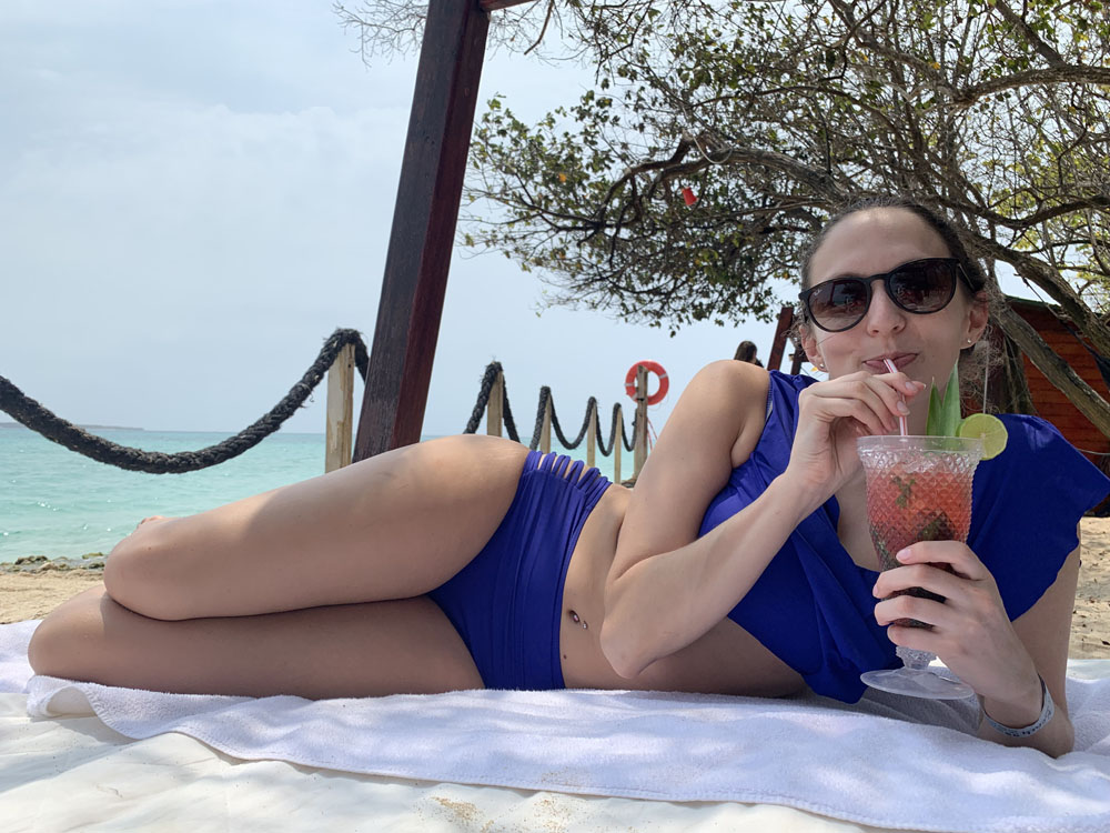 Lauren sitting. on a beach sipping a tropical drink on her trip to Colombia.