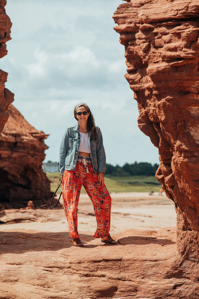 Girl on beach between big red rocks in Prince Edward Island.