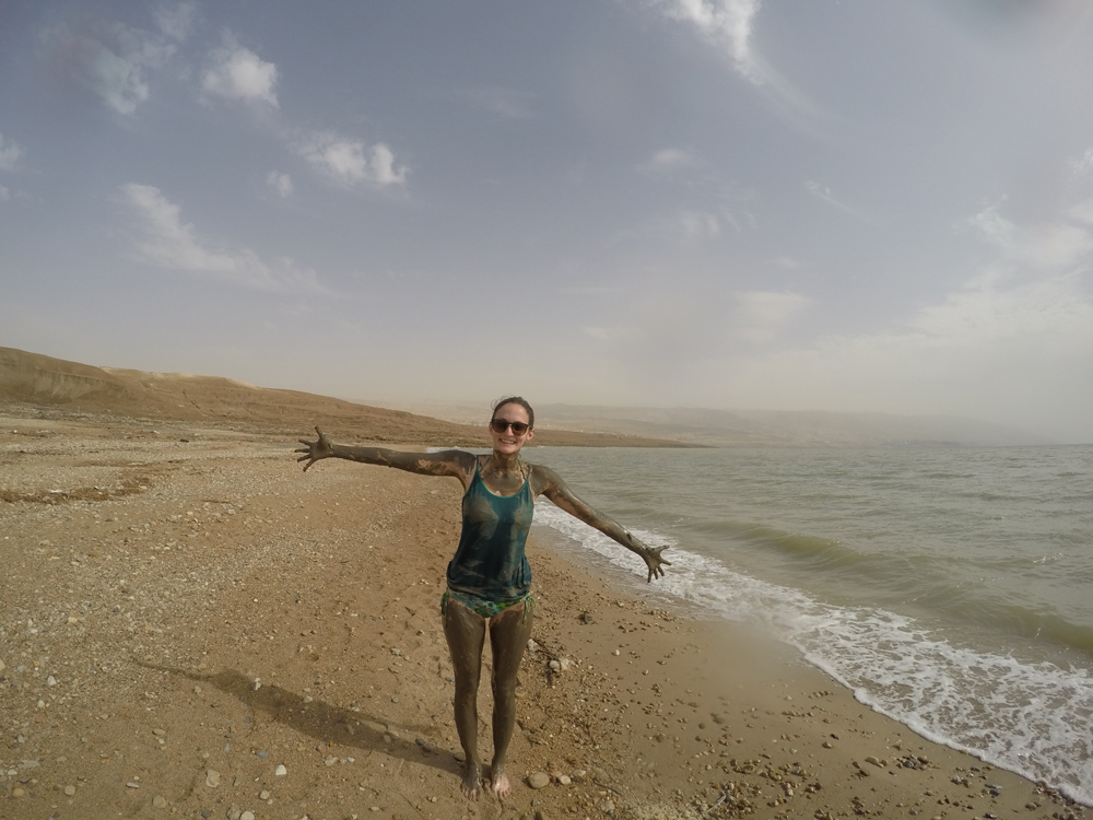 Girl covered in mud on a beach in Jordan next to the Dead Sea.