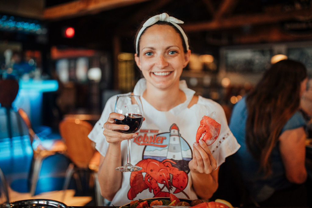 Girl posing with a lobster claw and red wine at a lobster dinner in PEI.